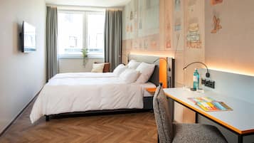 Una habitación de hotel con cama, escritorio, silla, televisor y ventana con cortinas.