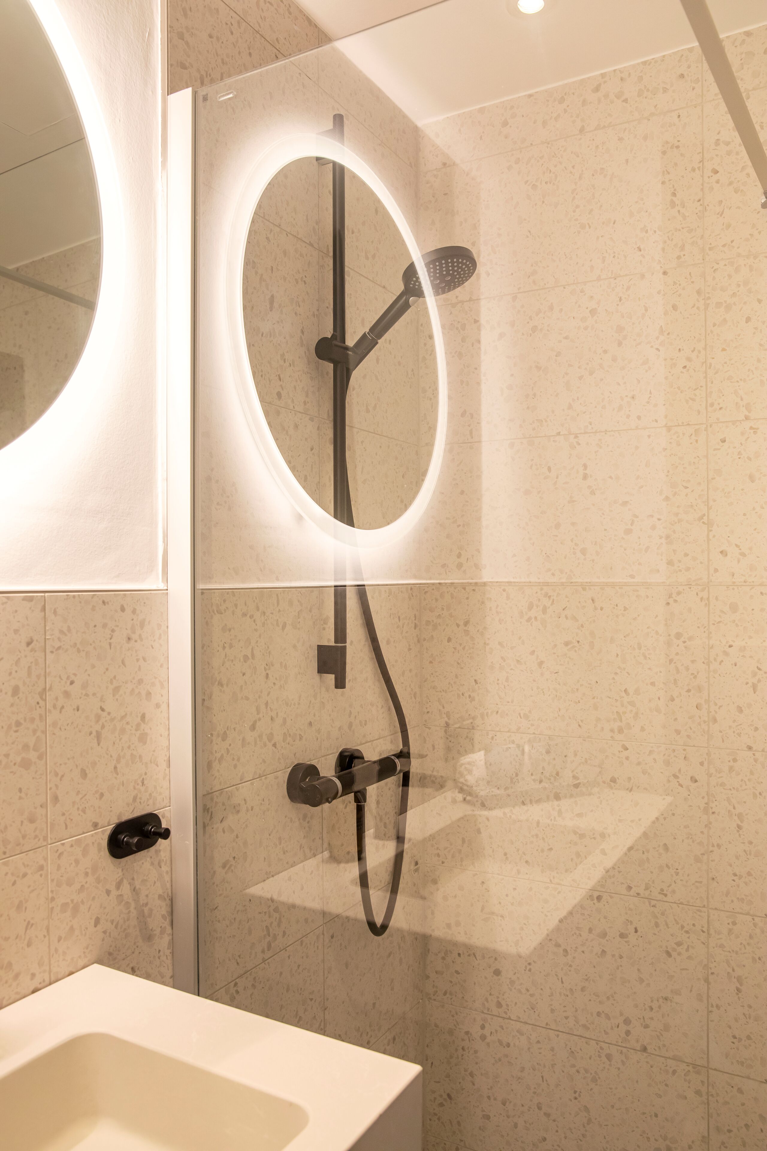Une salle de bain moderne avec une baignoire sur pieds, une douche à parois de verre et un grand miroir rond, ainsi que des toilettes fixées au mur.