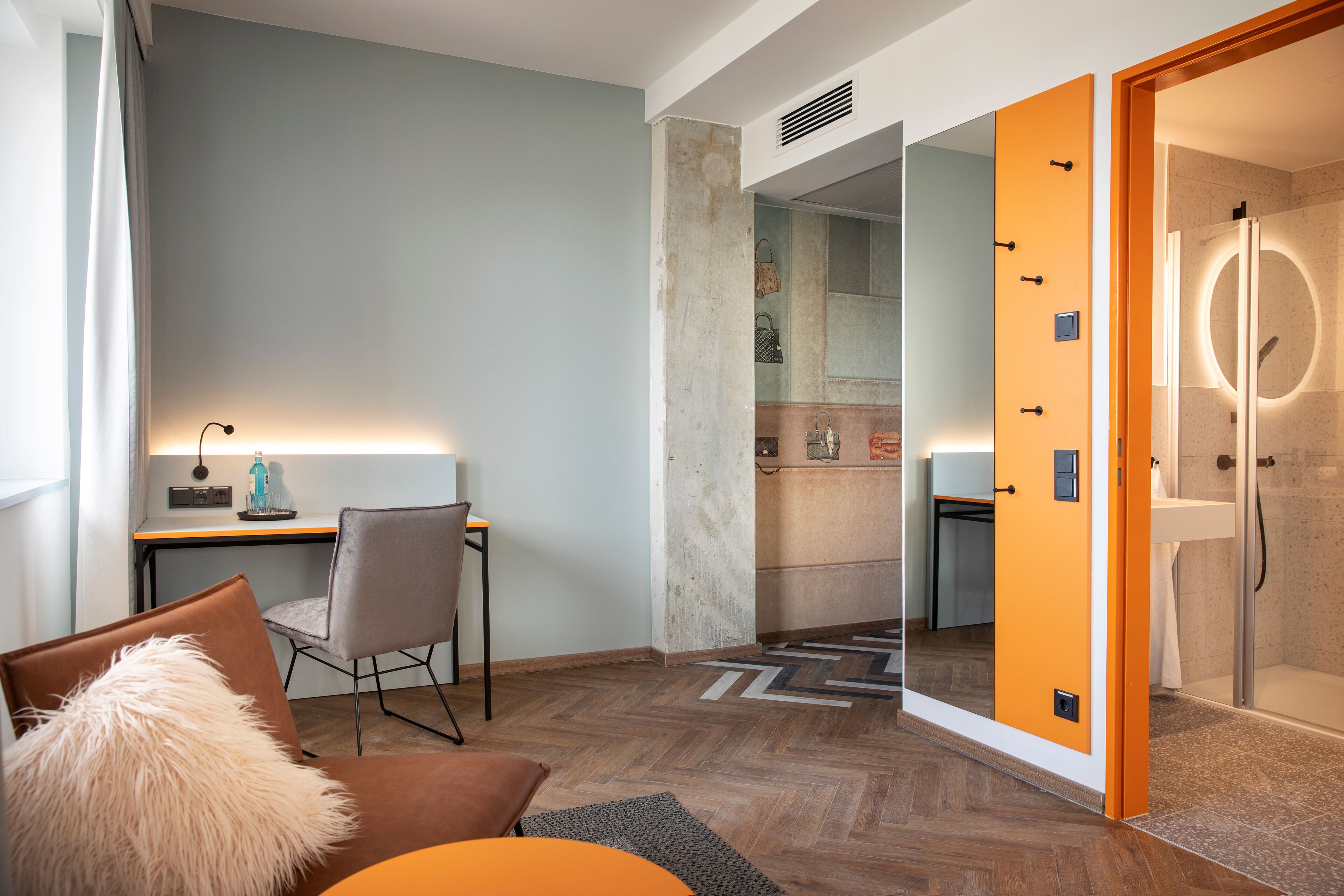 Una habitación de hotel moderna con suelo de madera, un escritorio con lámpara, una silla y un espejo grande.