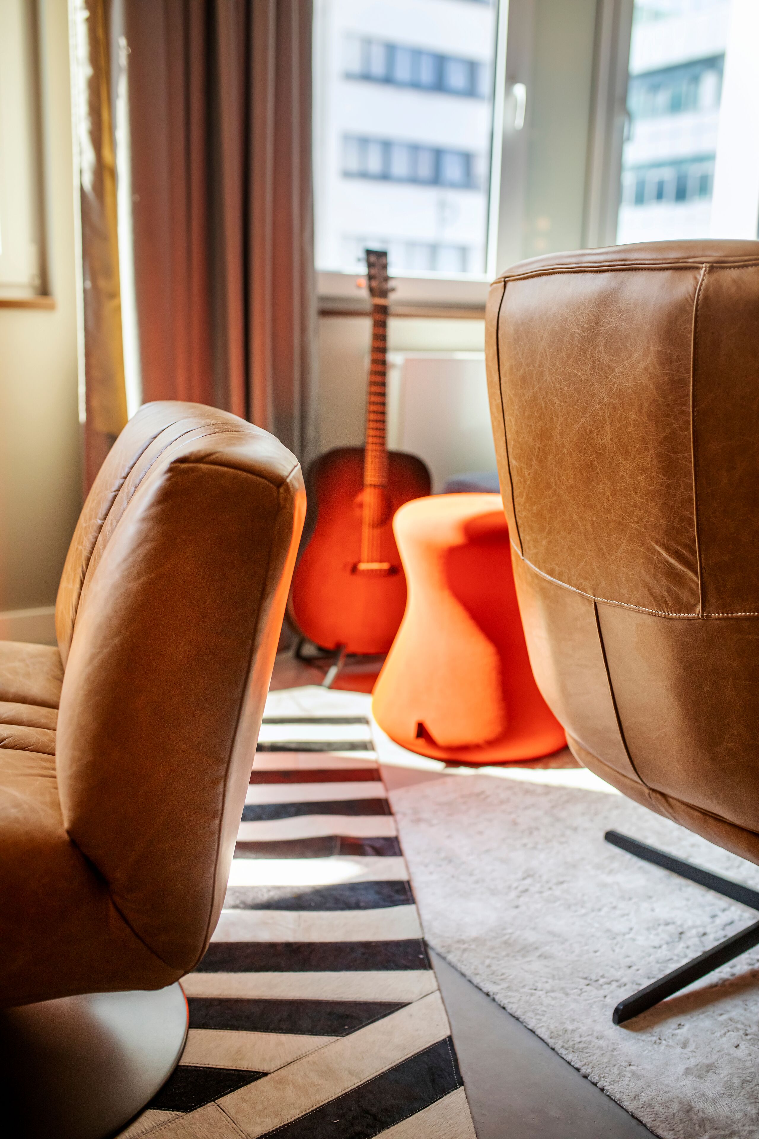 A modern living room with leather armchairs, a red guitar, and a patterned rug.