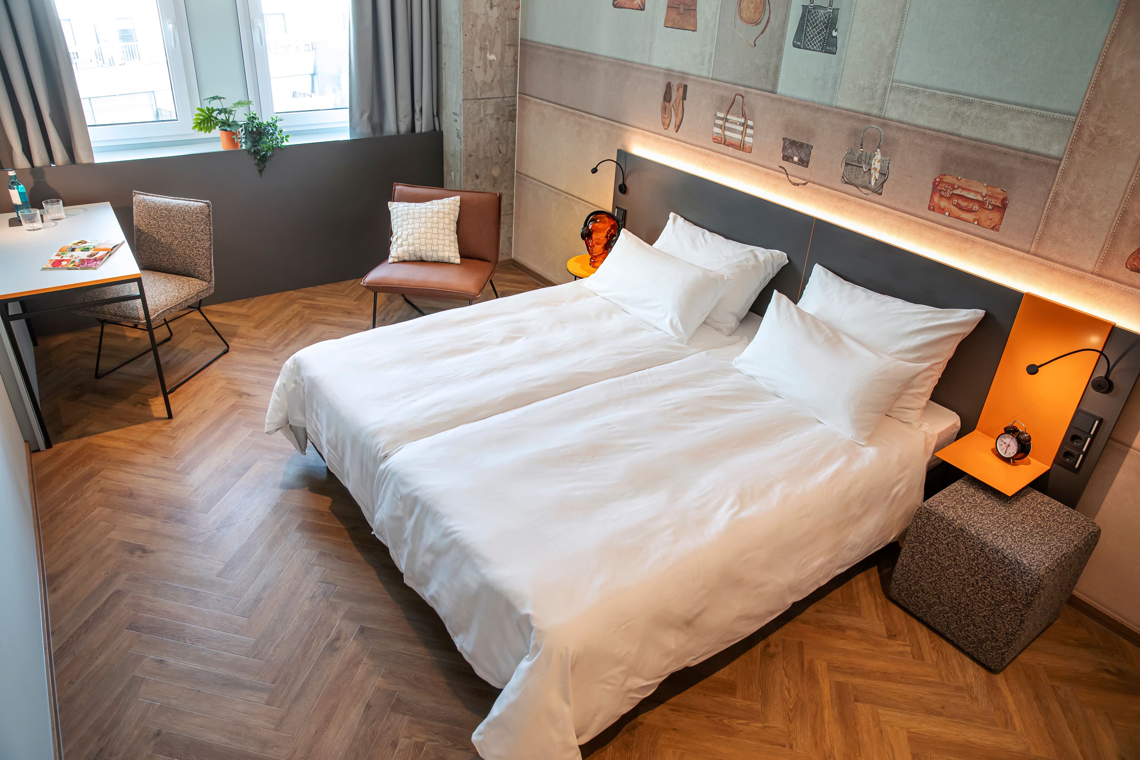 A hotel room with a large bed, a desk, and a chair. There is a potted plant on the windowsill.