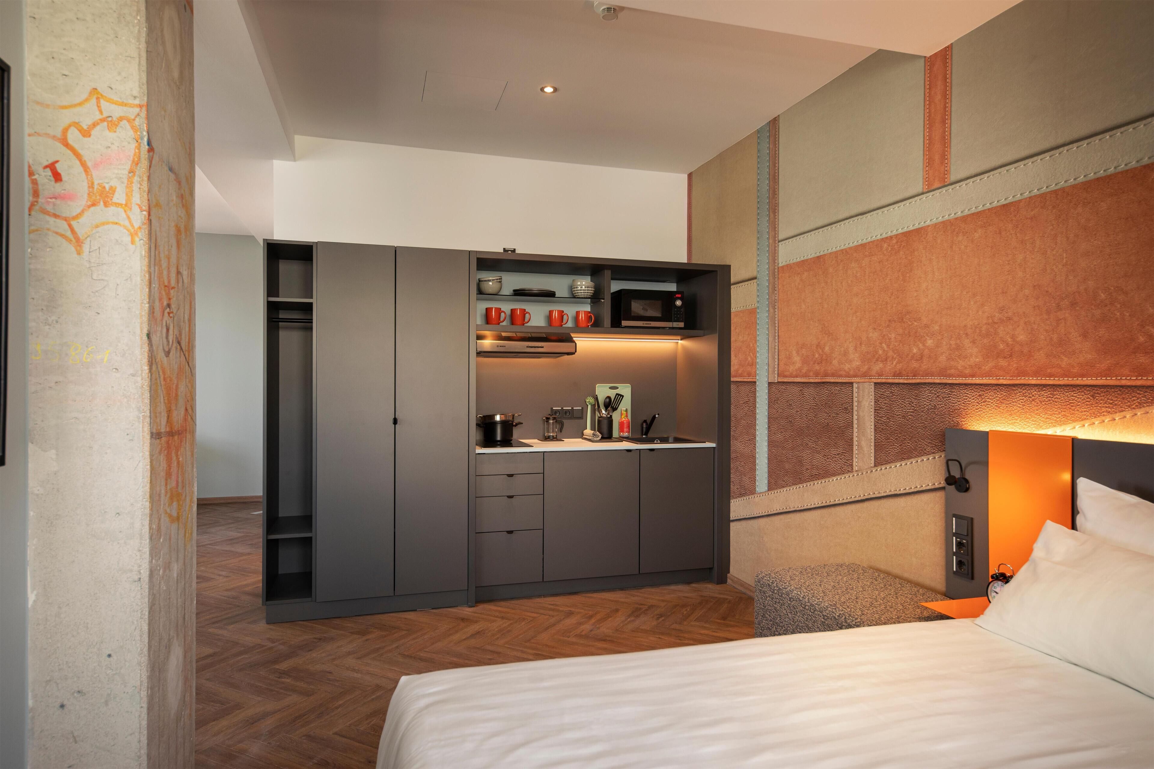 A compact hotel room with a bed, a kitchenette, and a built-in wardrobe.