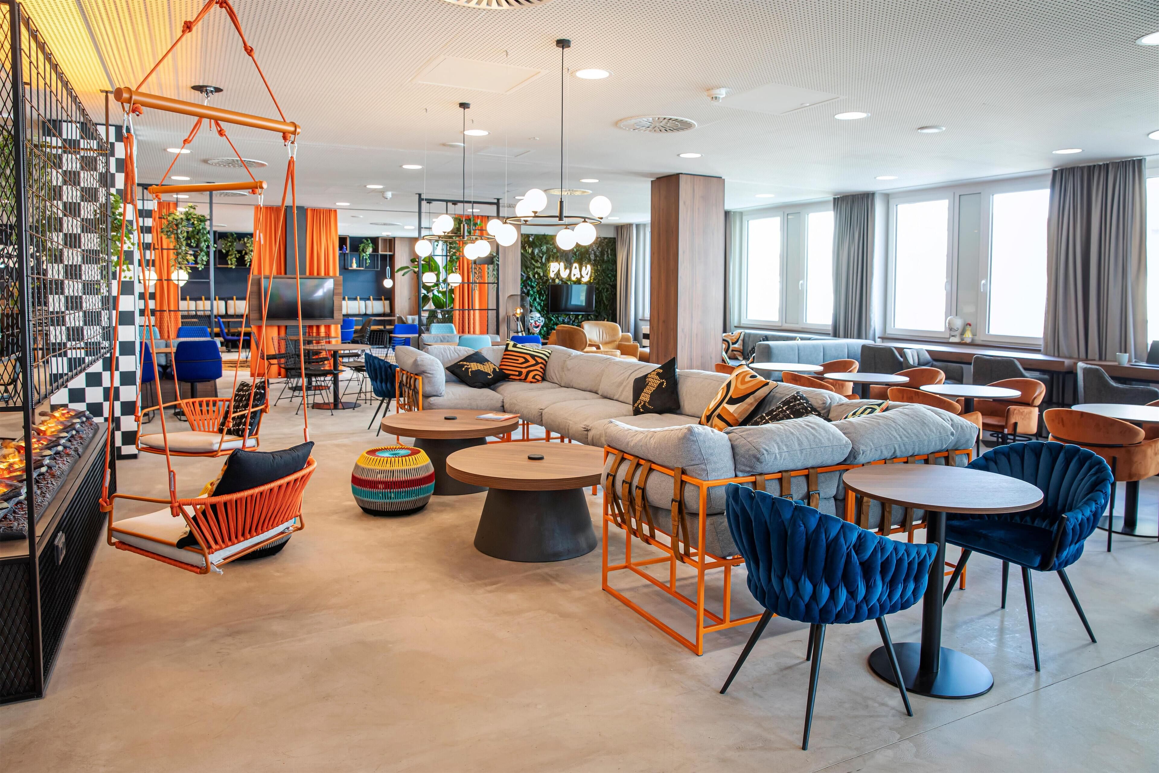 A modern lounge area with sofas, chairs, and tables, featuring a checkered wall and a hanging swing chair.