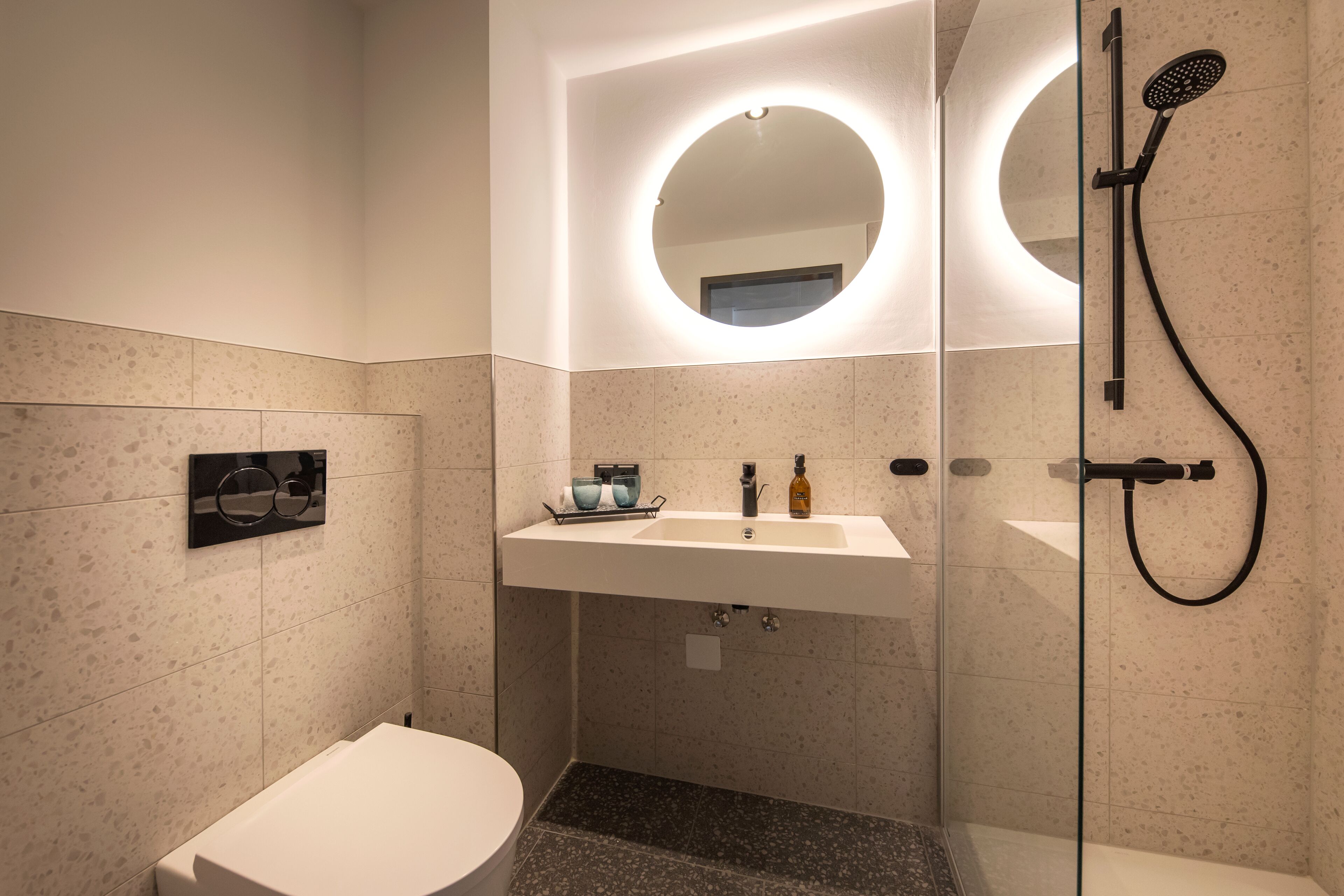 A modern bathroom with a round mirror, a sink, and a shower.
