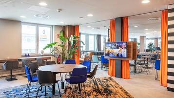 Un moderno vestíbulo de hotel con una mesa redonda, sillas azules, una planta grande y una pantalla de televisión.