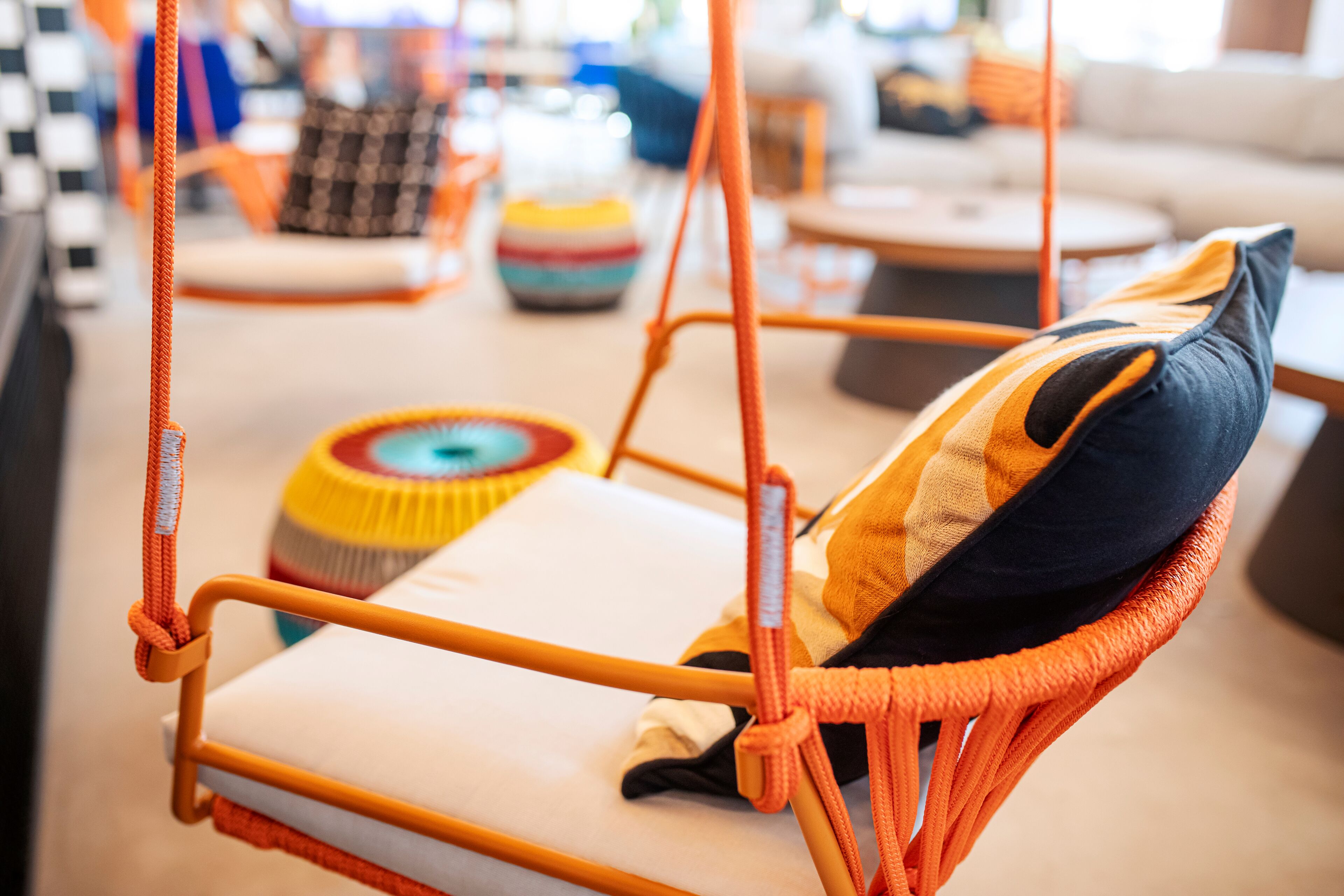 A wicker chair with a cushion and a hanging orange rope.