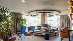 A modern lounge area with seating arrangements, a central pillar, and a view of the cityscape.