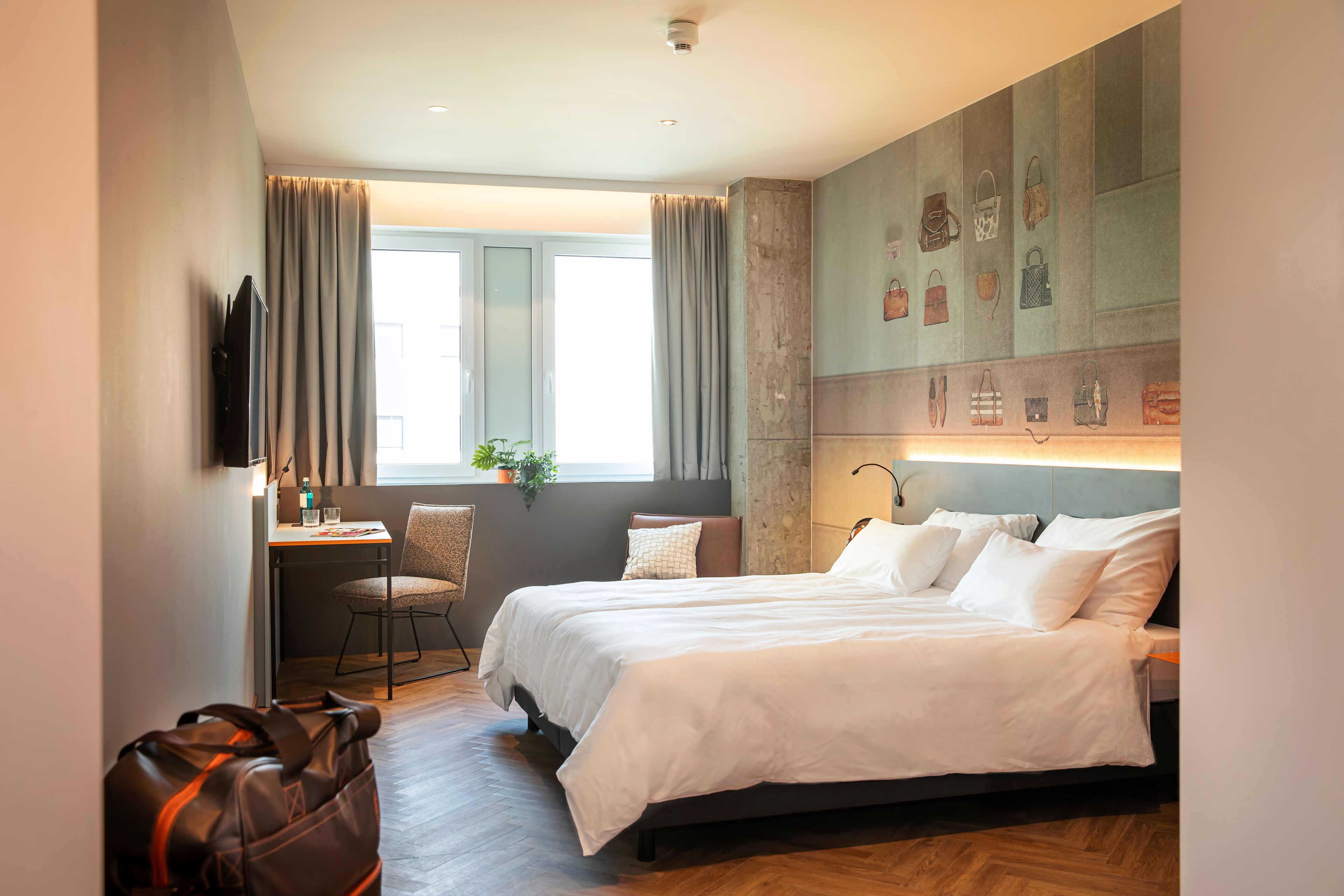 A hotel room with a large bed, a desk, a chair, and a wall-mounted TV.
