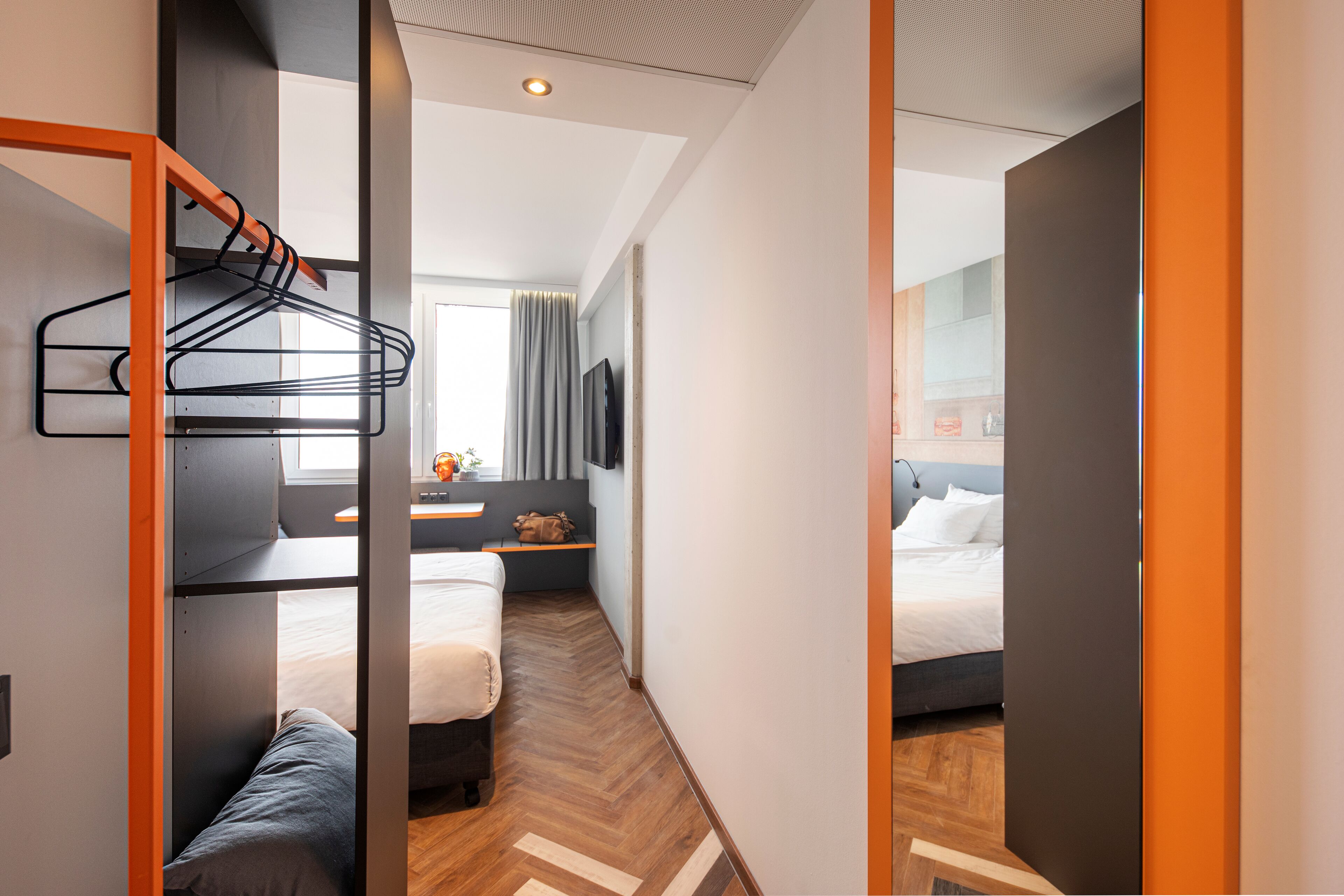 Una habitación de hotel moderna con una cama litera, un escritorio con silla, un televisor de pantalla plana y una ventana con cortinas.