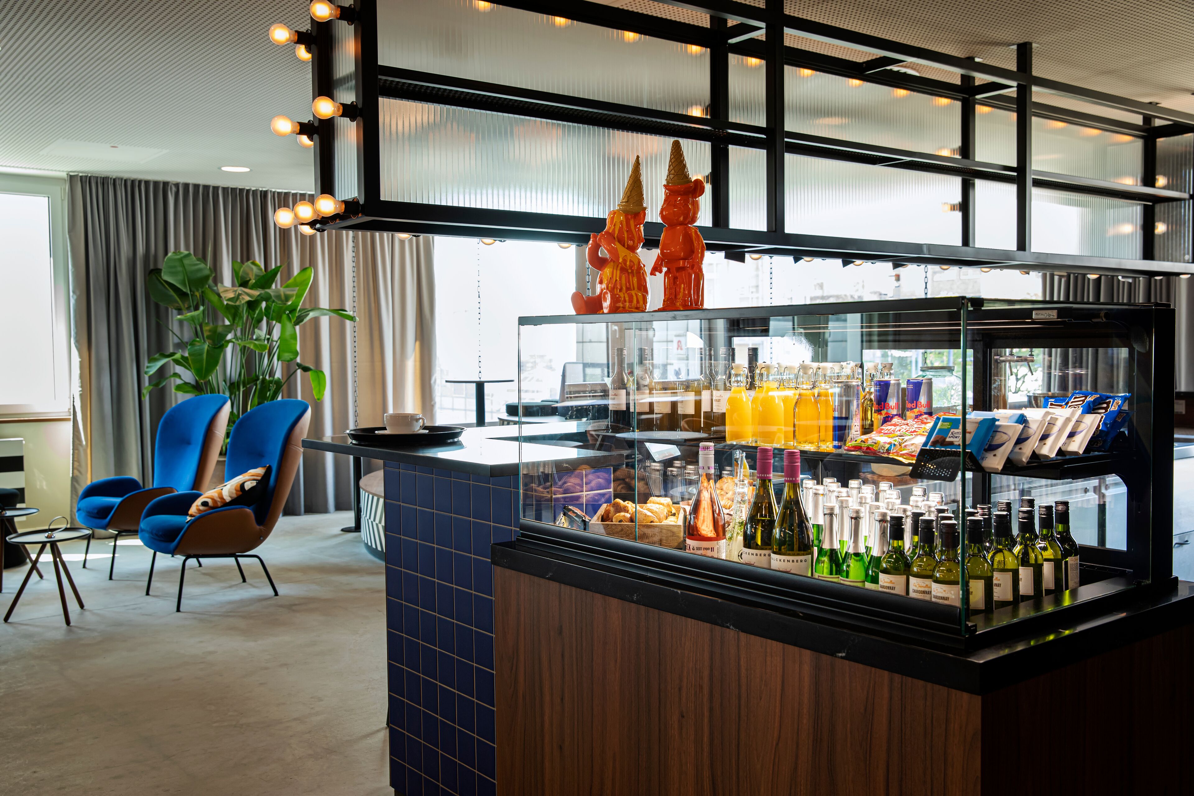A hotel lobby with a seating area, a bar with a glass display case, and a large window with curtains.