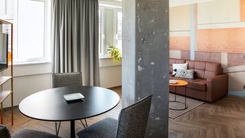 A modern living room with a round table, grey chairs, a brown leather sofa, and a large window with curtains.