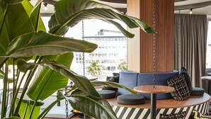 A modern lounge area with a circular seating arrangement, a hanging light fixture, and large green plants.