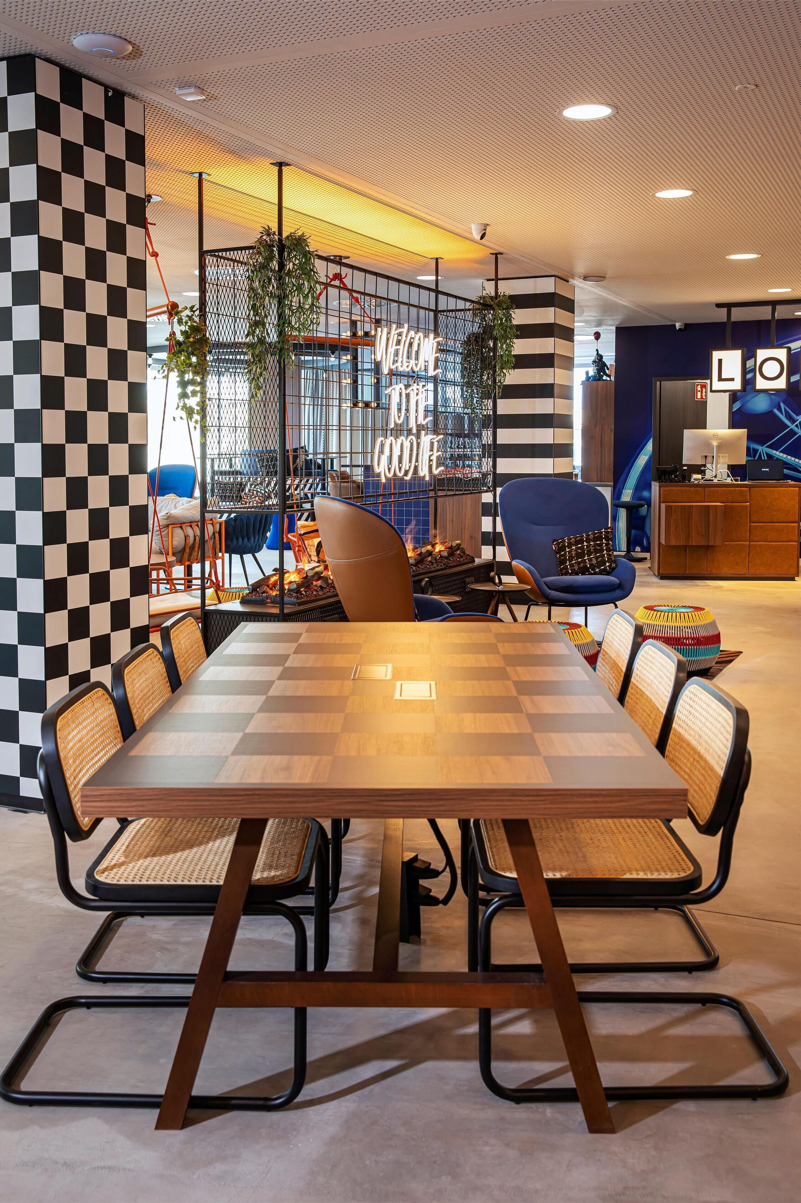 A modern meeting room with a large wooden table, black and white checkered walls, and comfortable seating.