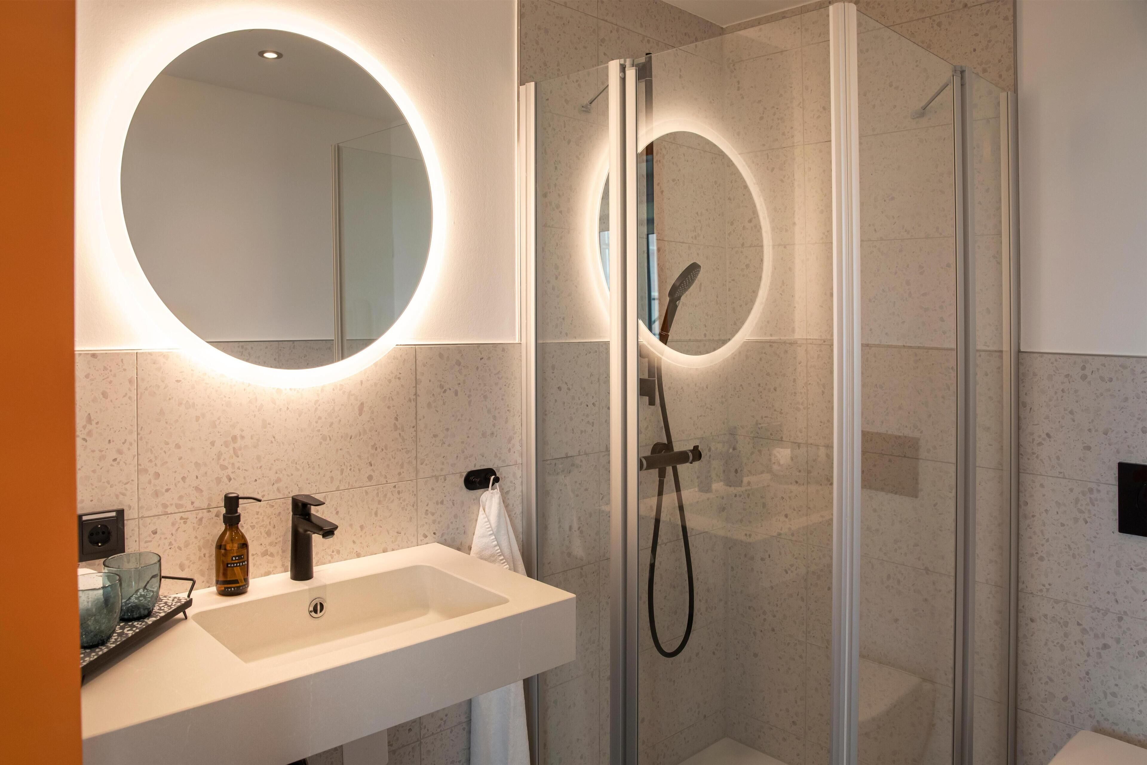 Ein modernes Badezimmer mit rundem Spiegel, Waschbecken und einer Duschkabine.