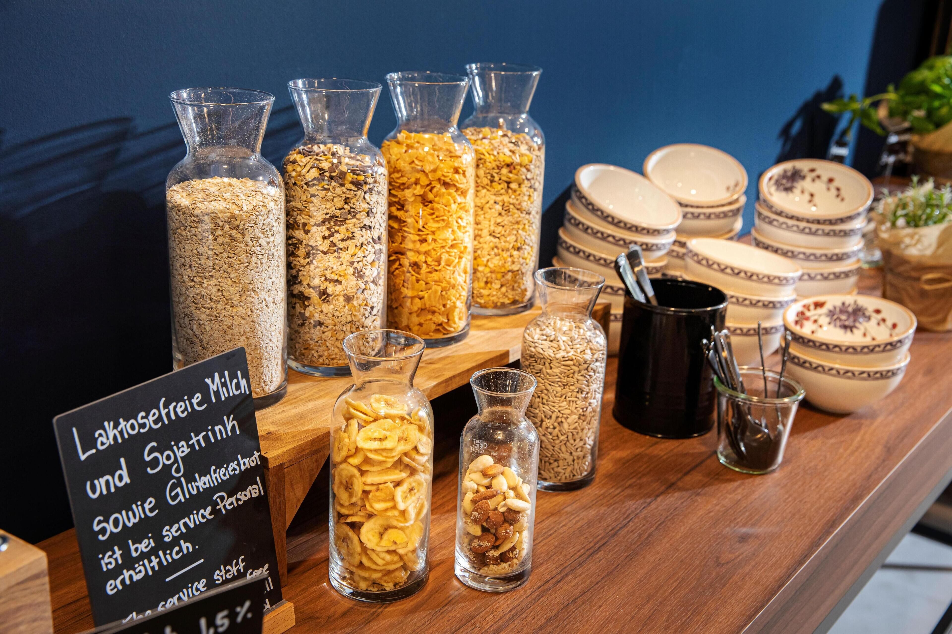 Un bufé de desayuno con diversos cereales y aperitivos en frascos y cuencos de vidrio.