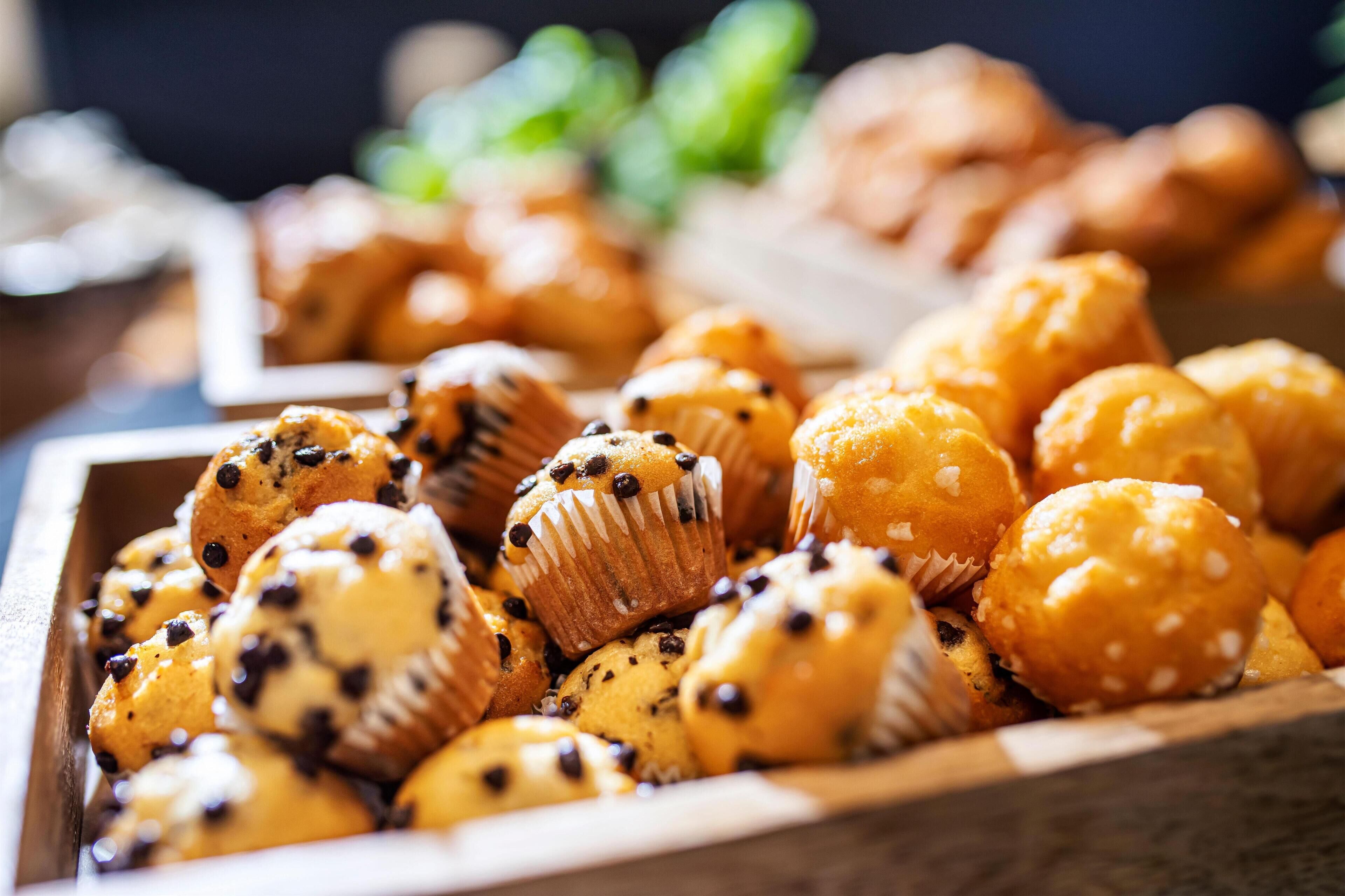A wooden tray filled with various muffins, some with chocolate chips and others with white toppings.