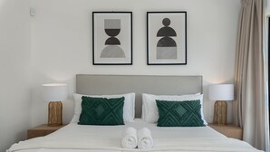 A neatly made bed with two pillows, a headboard, and two bedside tables with lamps. - Alexander Road 7B (Cape Town)