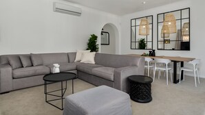 A modern living room with a grey sectional sofa, a small round table, and a dining area with a wooden table and white chairs. - Alexander Road 7B (Cape Town)