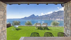 Una terraza con mesa de madera y cuatro sillas, con vista a un lago y montañas al fondo.