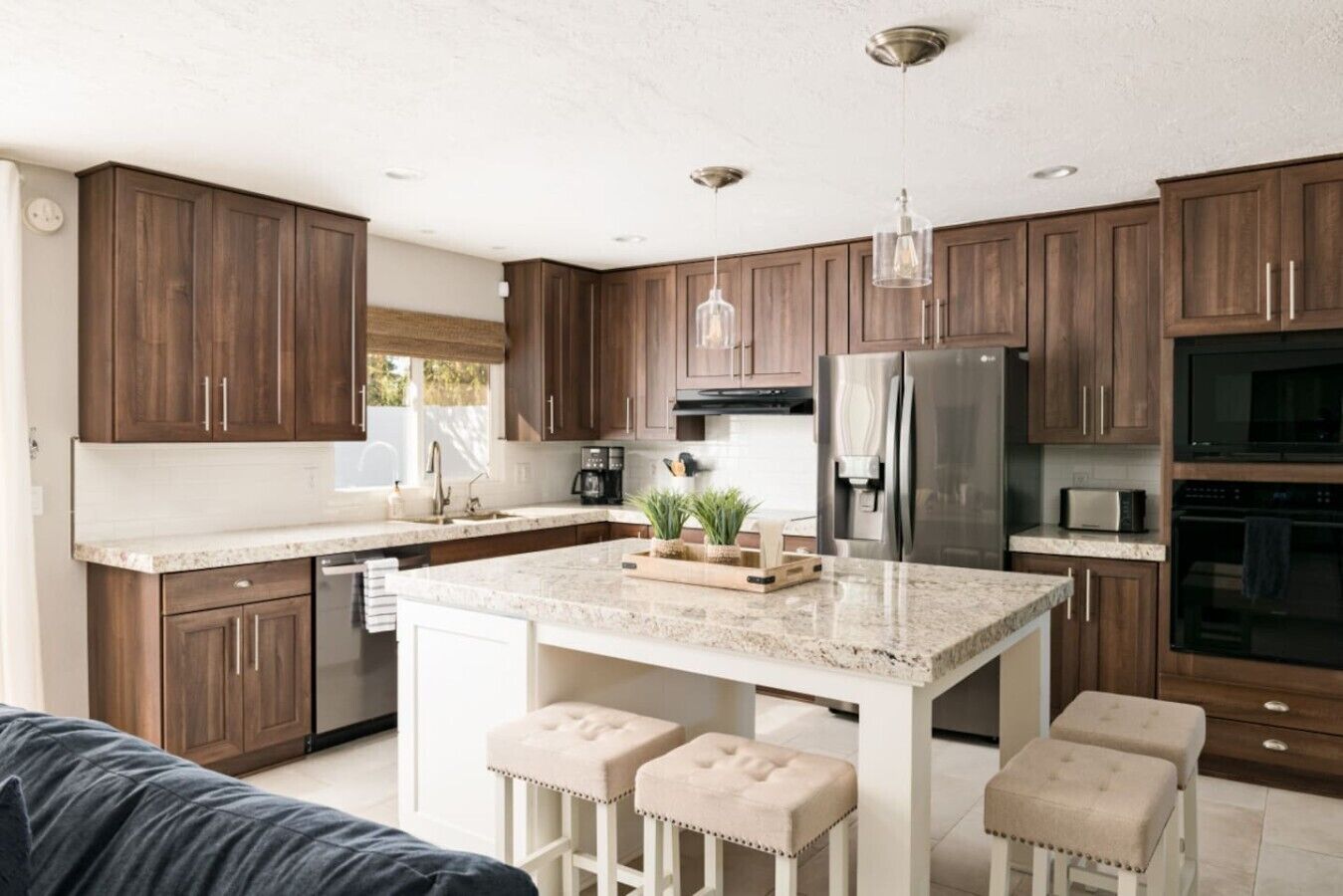 Une cuisine moderne avec des meubles en bois, des appareils en acier inoxydable, un plan de travail en marbre et des tabourets de bar.