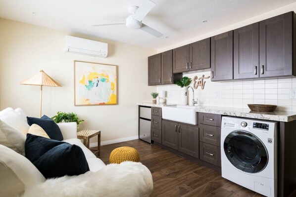 A modern kitchen with dark cabinets, a built-in washing machine, and a dining area with a white sofa and a painting.