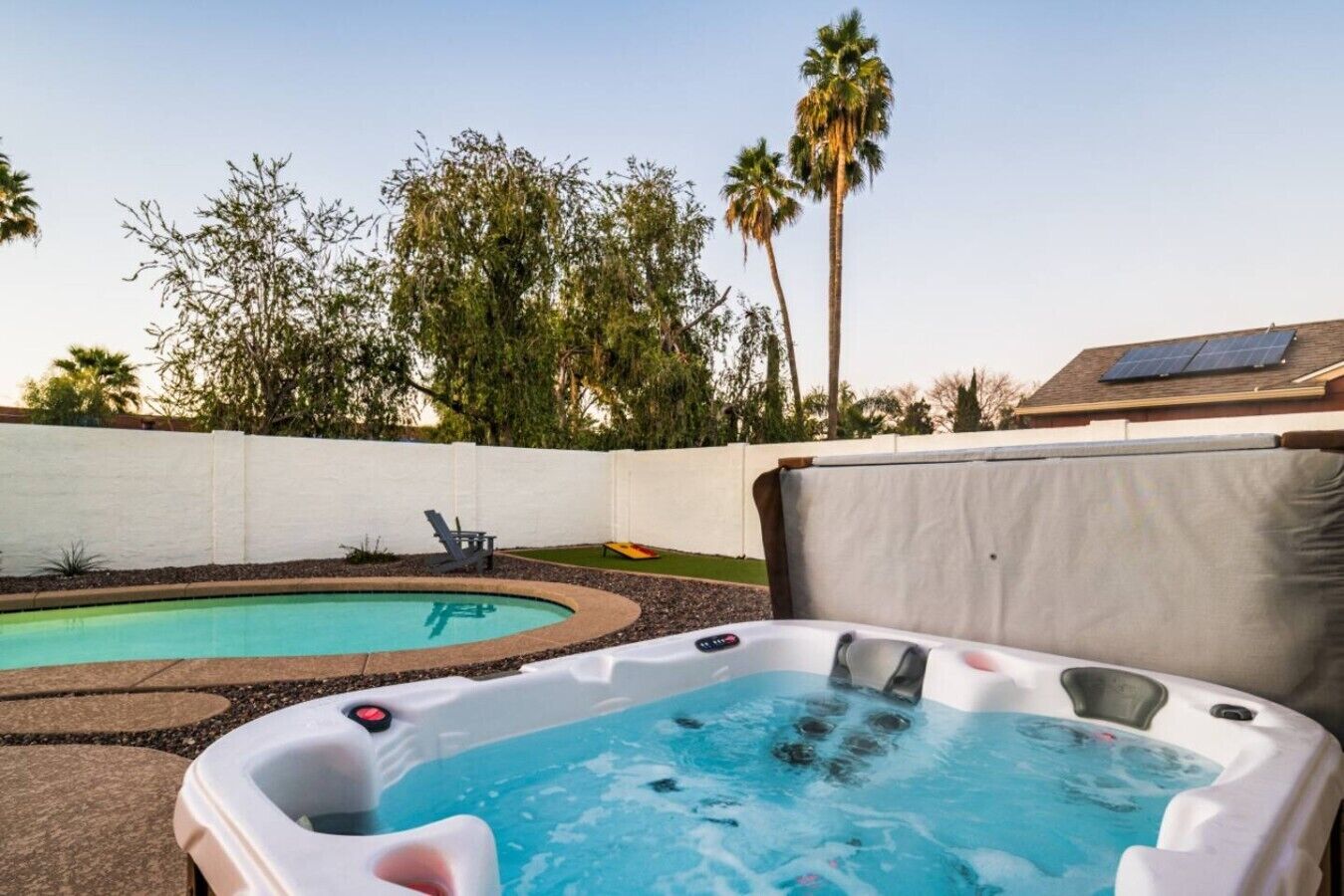 A backyard with a hot tub, a swimming pool, and a white fence.