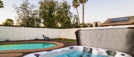 Un patio trasero con jacuzzi, piscina y cerca blanca.
