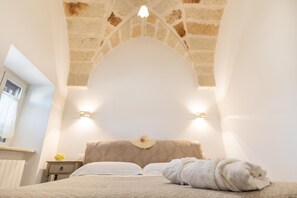 Un dormitorio con techo de piedra, una cama con ropa blanca y una mesita de noche con una lámpara.