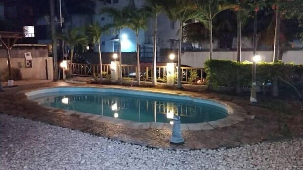 A swimming pool with a paved deck, surrounded by palm trees and a building with illuminated windows.