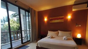 A hotel room with a large bed, two bedside lamps, a window with a view of the outside, and an air conditioning unit on the wall.
