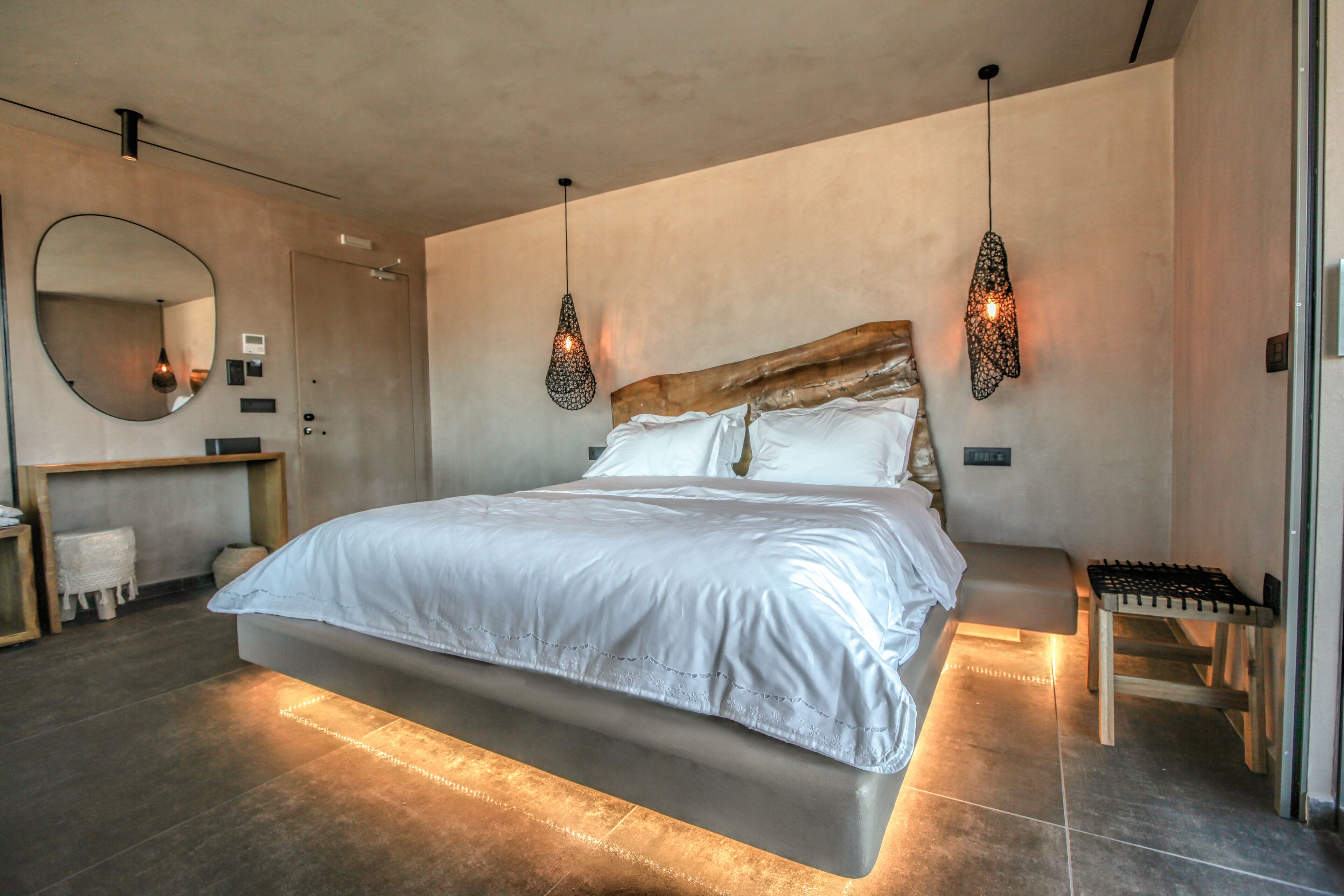 A modern bedroom with a large bed, bedside tables, a mirror, and pendant lights.