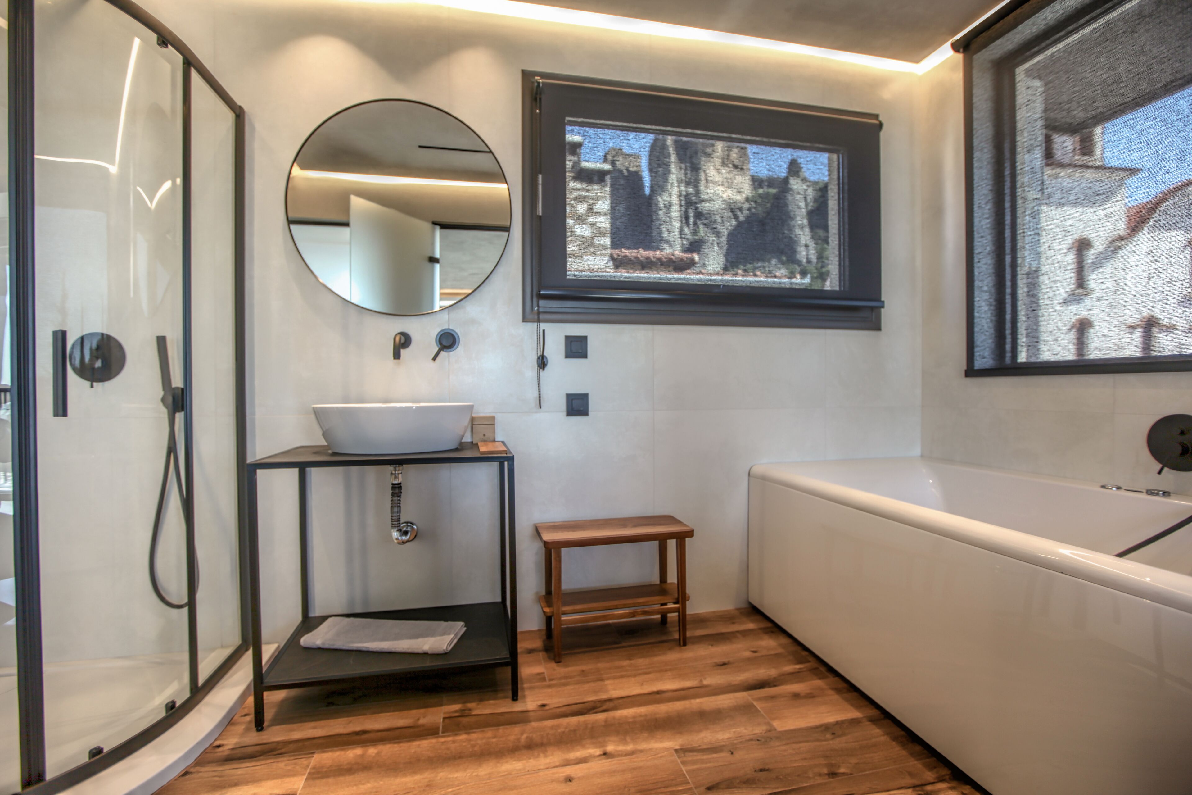 Une salle de bain moderne avec une douche à parois de verre, un lavabo avec un miroir, un petit tabouret en bois et une baignoire.