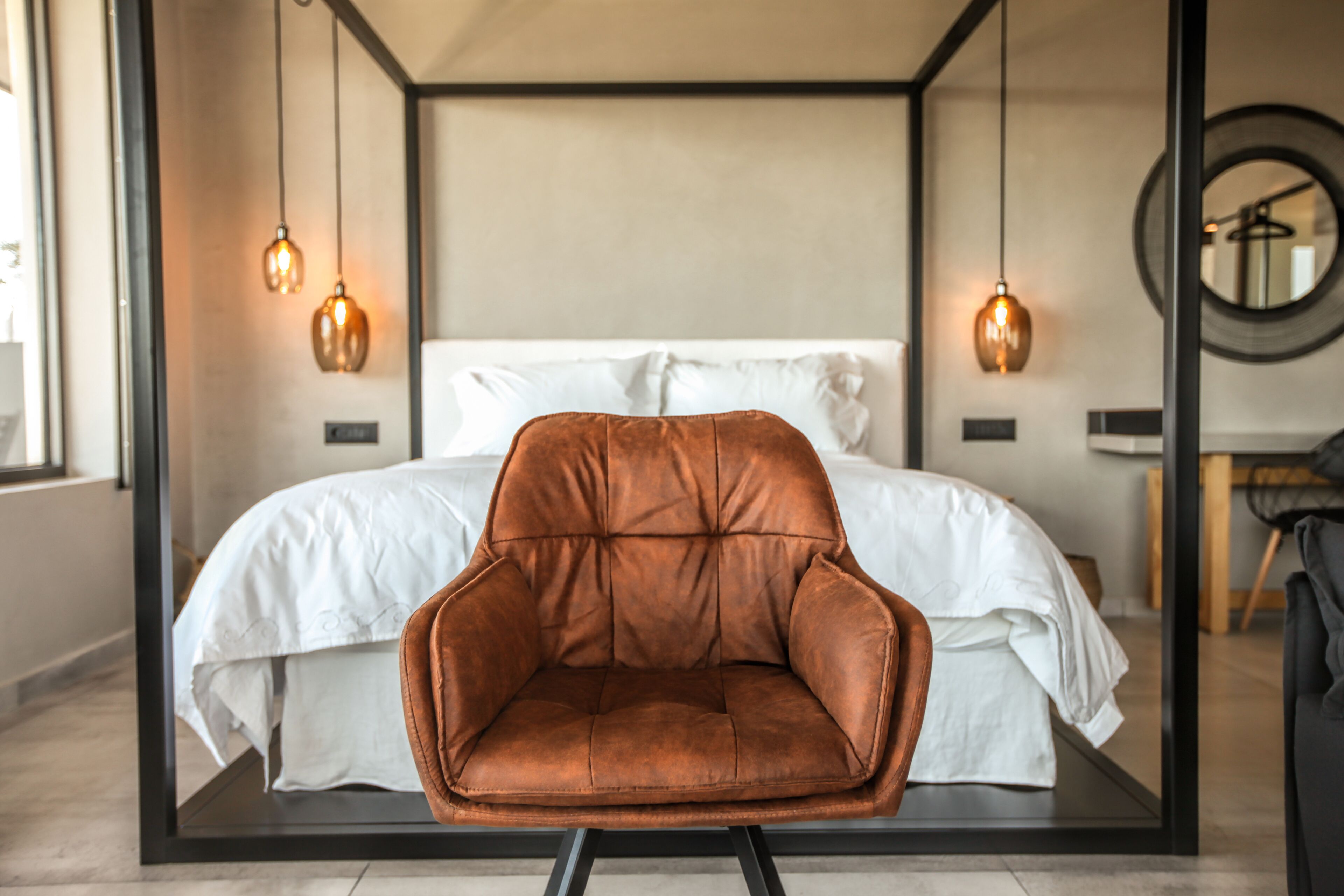 A modern bedroom with a large bed, a brown leather chair, and pendant lighting.