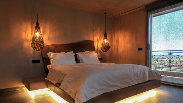 A modern bedroom with a large bed, two hanging light fixtures, and a view of the outdoors through a window.
