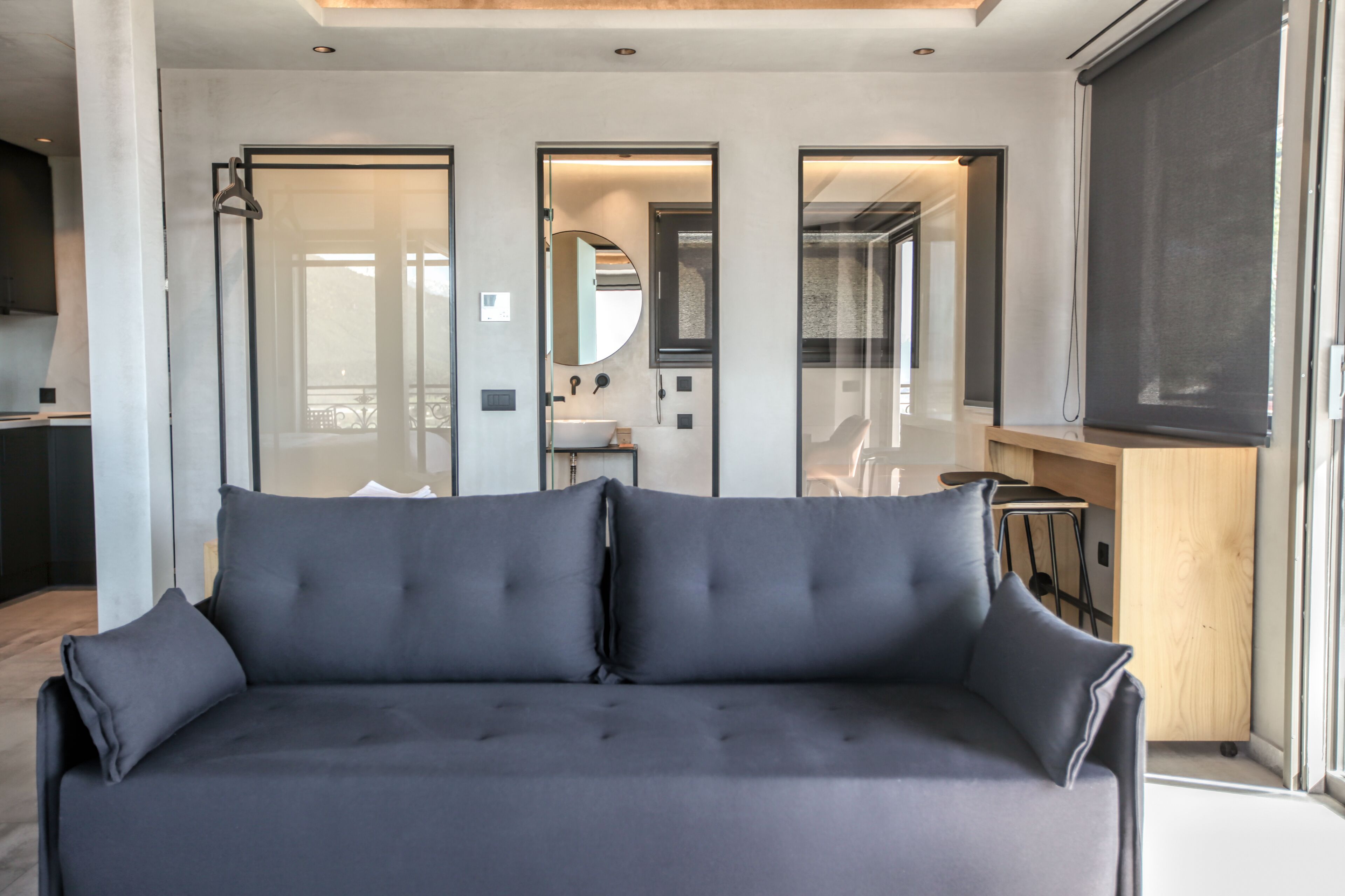 Un salon moderne avec un canapé gris, une table d’appoint en bois et une vue sur la cuisine à travers des portes vitrées.