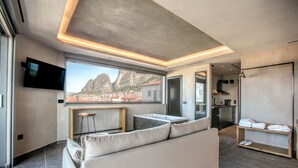 A modern living room with a large window, a sofa, a TV, and a kitchen area.