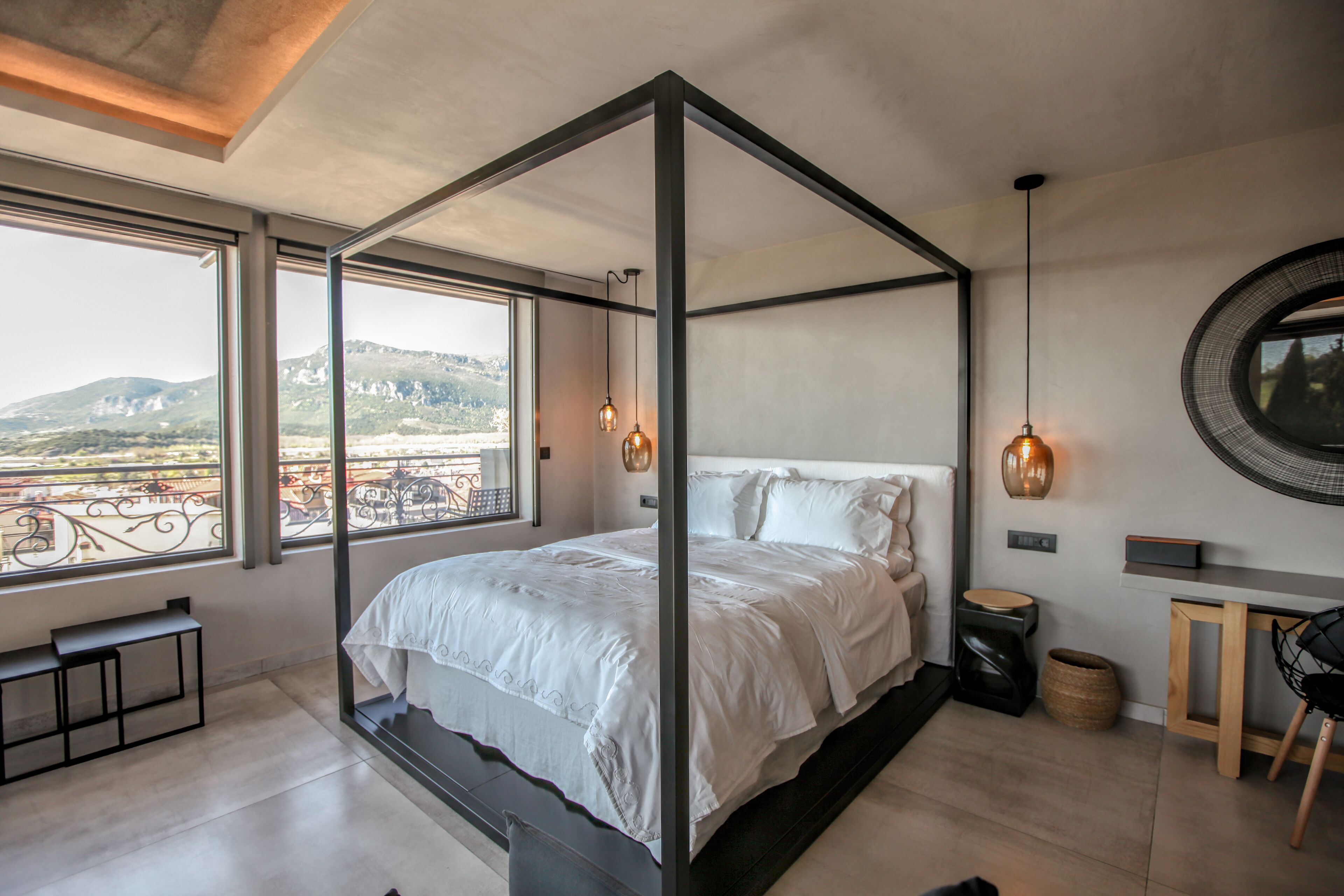 A modern bedroom with a four-poster bed, large windows, and a view of the city.