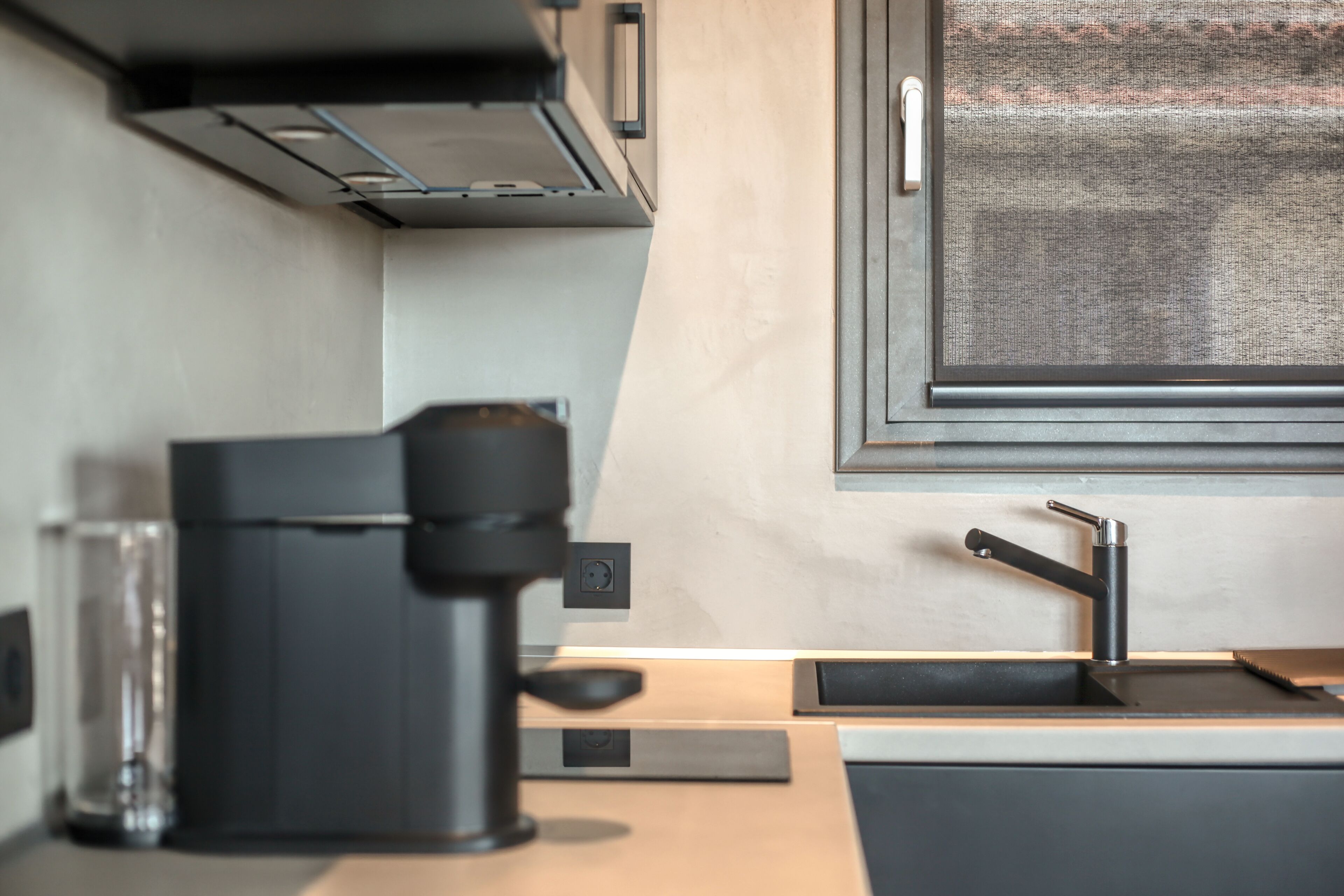 A modern kitchen with a built-in coffee maker, a sink, and a window with a view of the outdoors.