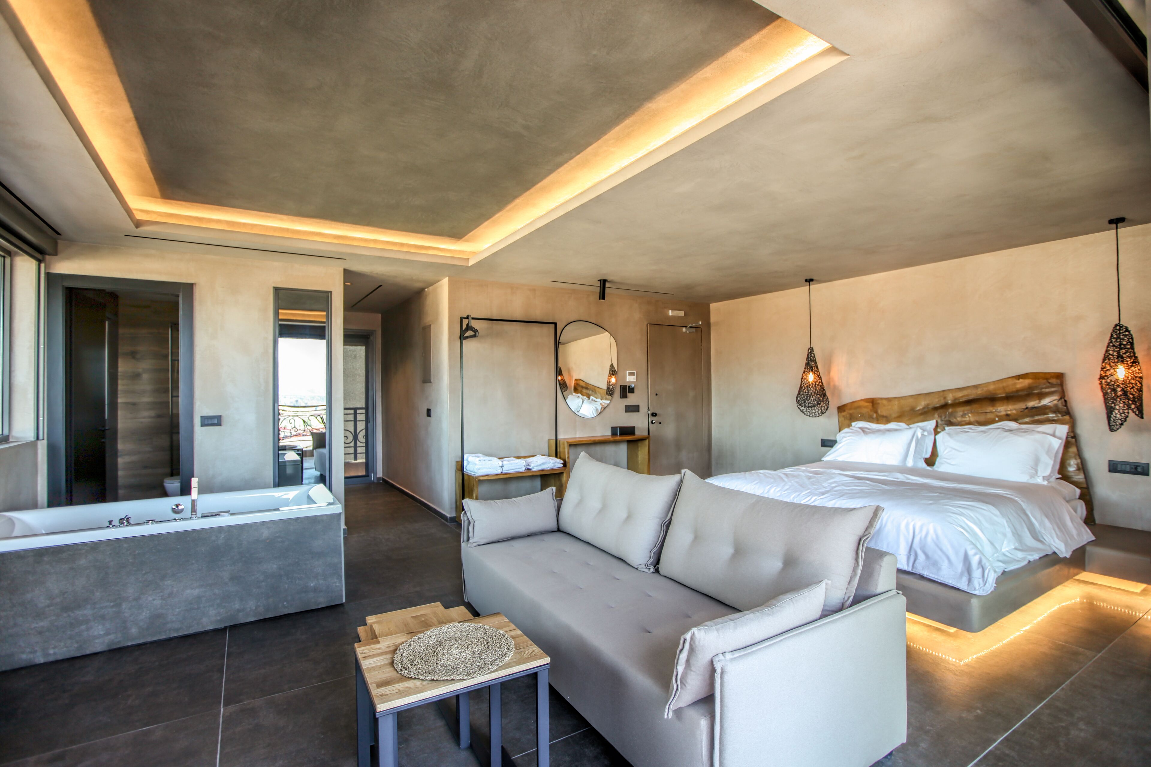 A modern bedroom with a large bed, a sofa, a bathtub, and a mirror.