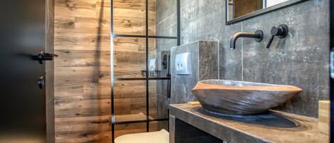 A modern bathroom with a wooden floor, a large mirror, a vessel sink, and a toilet.