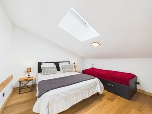 A bedroom with a skylight, a bed with a red blanket, a bedside table with a lamp, and a small desk with a lamp. - Chic Apartment with Balcony, 2 Bedrooms & Mountain Views in Les Gets (Les Gets)