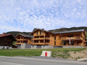 A wooden lodge with multiple balconies and a stone foundation, set against a backdrop of hills and a clear sky. - Chic Apartment with Balcony, 2 Bedrooms & Mountain Views in Les Gets (Les Gets)
