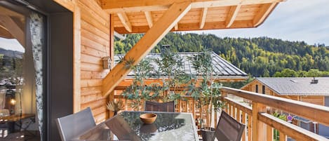 A wooden deck with a glass table and chairs, overlooking a forested area.