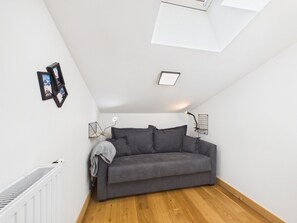 A room with a grey sofa, white walls, a wooden floor, a skylight, and a radiator. - Chic Apartment with Balcony, 2 Bedrooms & Mountain Views in Les Gets (Les Gets)