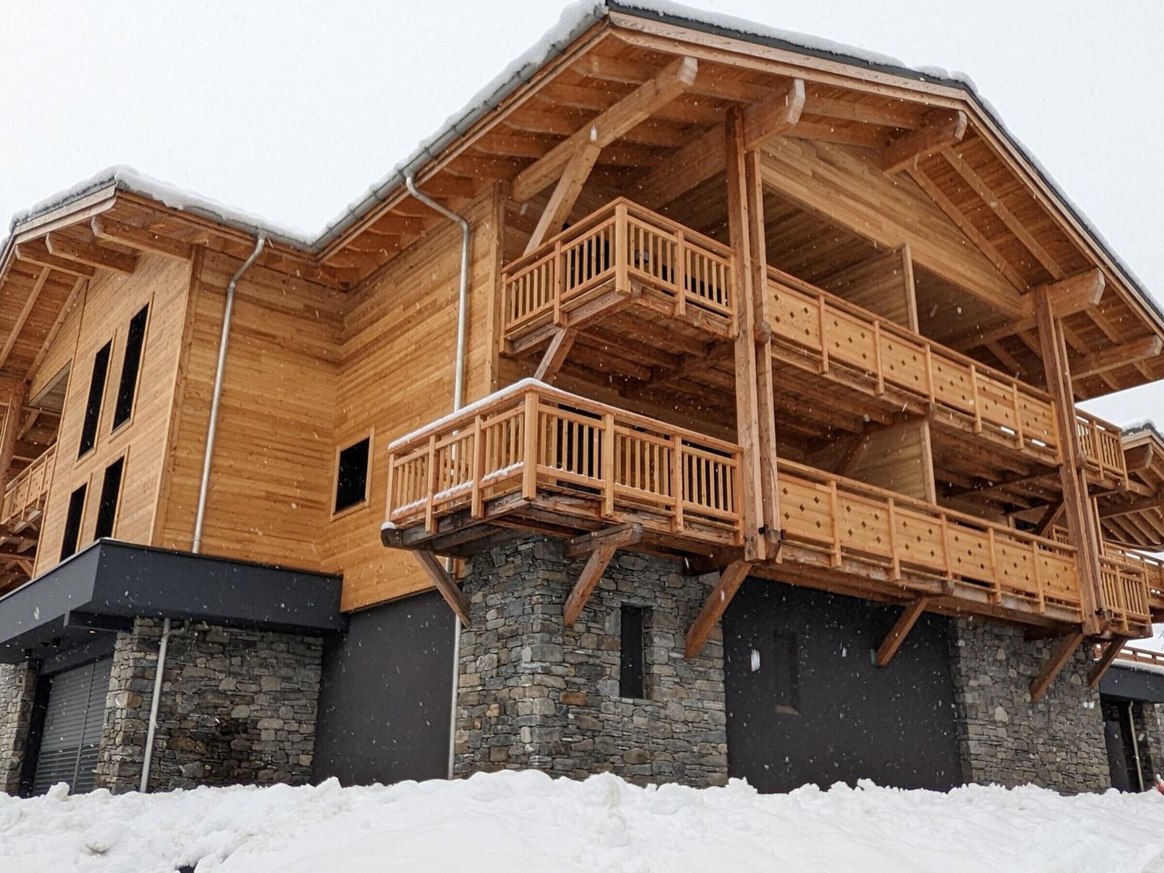 Una cabaña de madera con cimientos de piedra, varios balcones y techo cubierto de nieve.