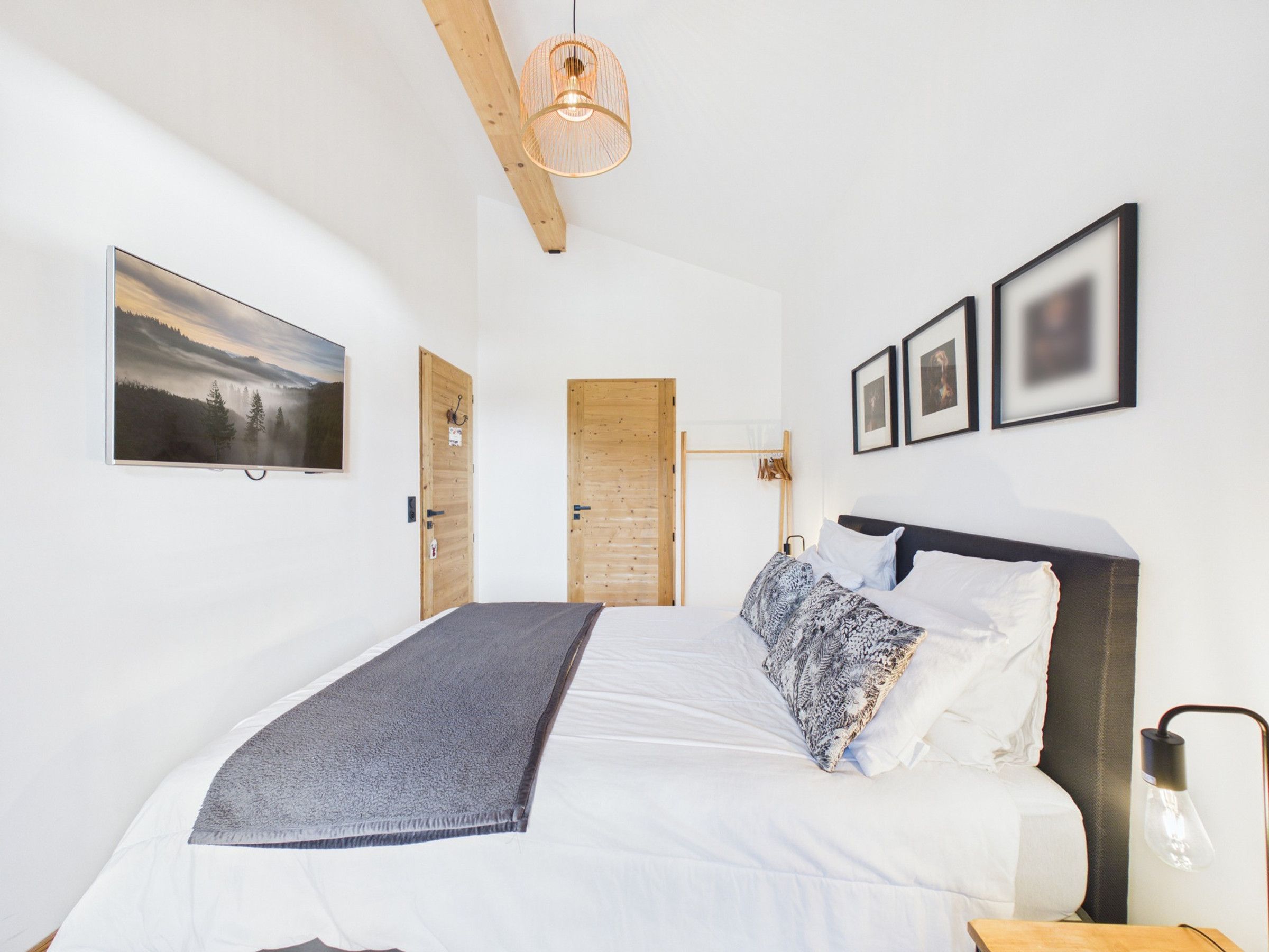 A bedroom with a bed, a hanging light fixture, a wall-mounted picture, and a door.