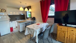 Una cucina compatta con angolo ristoro, TV e finestra con tende rosse.