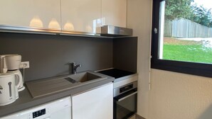 Una cucina compatta con mobili bianchi, un forno integrato, una macchina per il caffè e una finestra che si affaccia su un giardino.