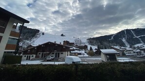 Un villaggio montano innevato con edifici in stile chalet, una pista da sci sullo sfondo e un cielo nuvoloso.