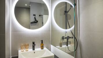 Un baño moderno con un lavabo blanco, dos vasos, un dispensador de jabón y un espejo con luz circular.